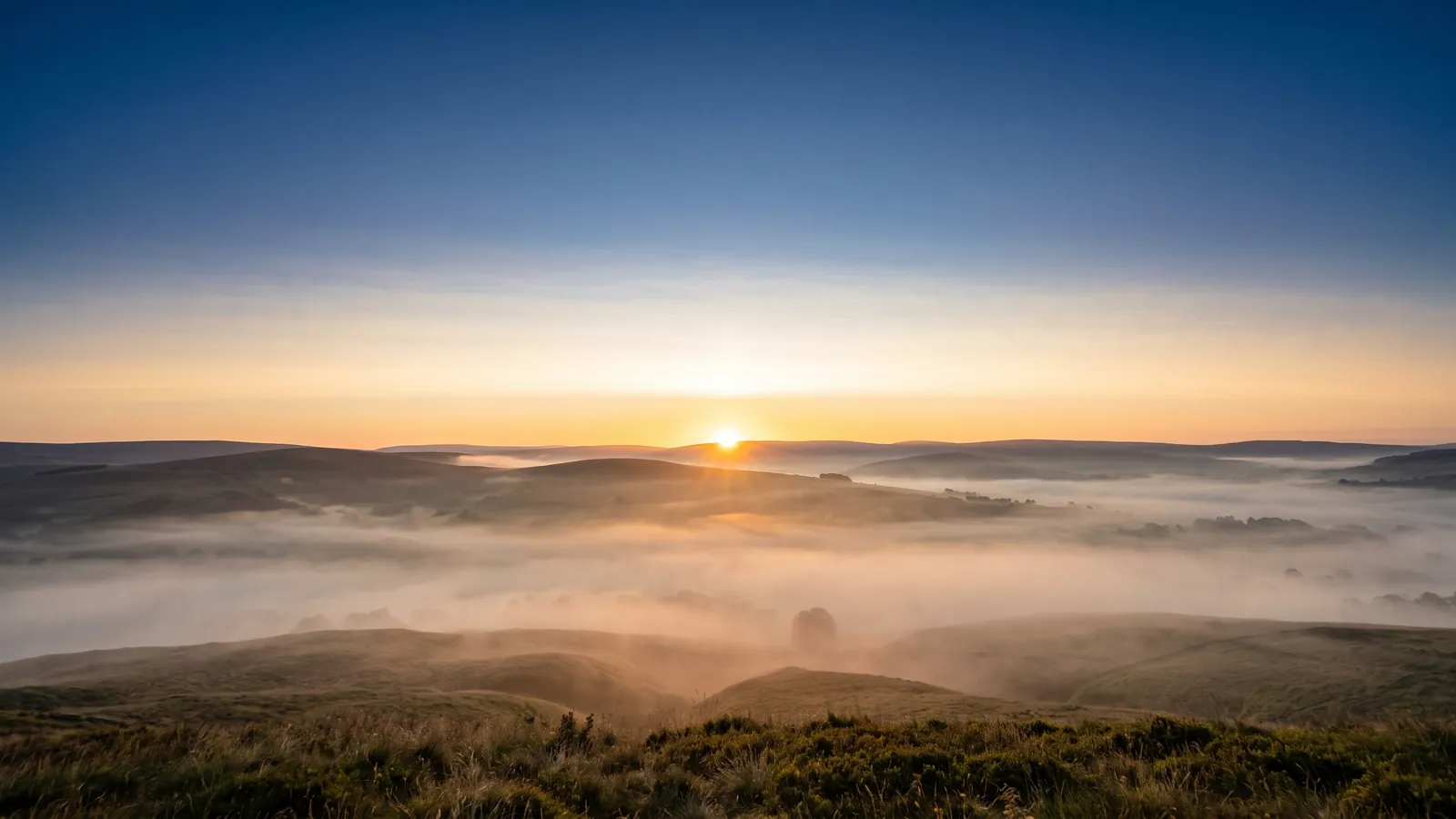 Le Soleil qui se lève pile sur l'horizon à l'est, au-dessus de collines, dans un ciel d'aube pêche.