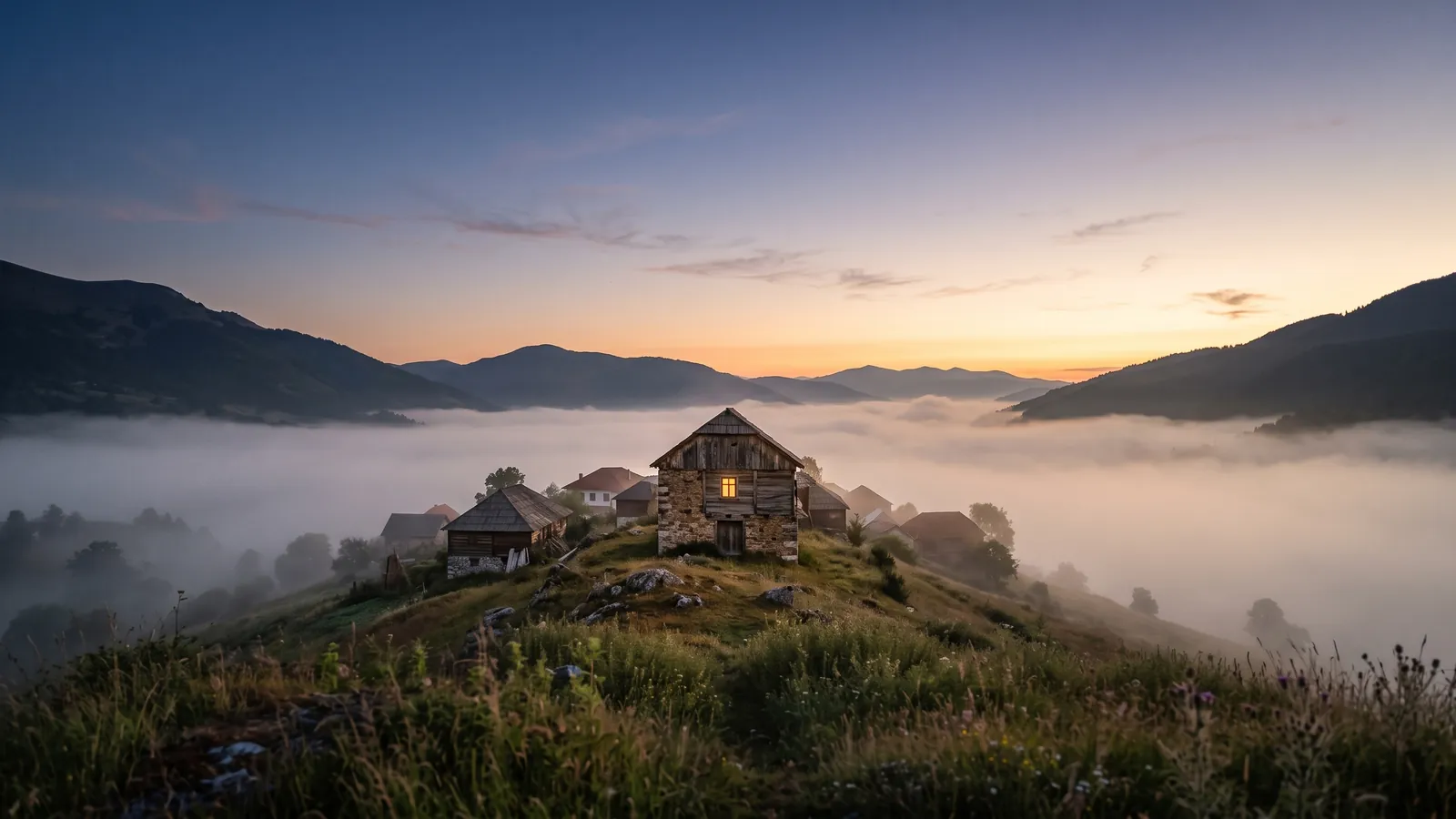 Un village de montagne des Balkans à l'aube, de la brume dans la vallée et une fenêtre éclairée.